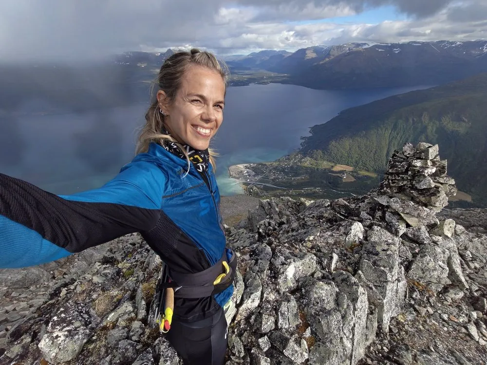 Anne Mjelva på en fjelltopp med fjorden bak seg.